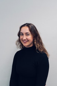 a woman in a black turtle neck top smiling against a white wall